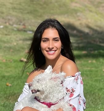 Jessica smiling outdoors while holding her white dog, Bella, as they enjoy a sunny day in the park.